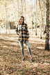 © Mila - A beautiful girl in jeans and a plaid shirt walks in a birch grove. Portraits of a brunette girl in nature, in the autumn forest