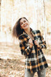© Mila - A beautiful girl in jeans and a plaid shirt walks in a birch grove. Portraits of a brunette girl in nature, in the autumn forest