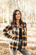 © Mila - A beautiful girl in jeans and a plaid shirt walks in a birch grove. Portraits of a brunette girl in nature, in the autumn forest