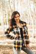 © Mila - A beautiful girl in jeans and a plaid shirt walks in a birch grove. Portraits of a brunette girl in nature, in the autumn forest