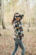 © Mila - A beautiful girl in jeans and a plaid shirt walks in a birch grove. Portraits of a brunette girl in nature, in the autumn forest