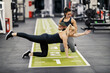 © Dusan Petkovic - A fit sportswoman is doing exercises in a gym while her female coach is tracking progress on a tablet.