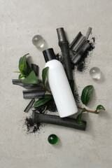 An unlabeled bottle of shower gel is placed on bamboo charcoal and green tea leaves against a gray background and transparent spheres. Branding a natural cosmetics.