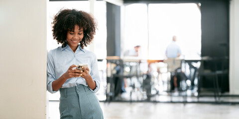 Smiling african american businesswoman using smart phone leaning at office