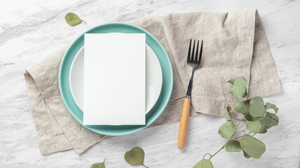 Wall Mural - Wedding menu card on plate with fork on linen napkin on marble table with green leaves