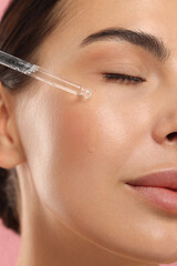 Poster - Beautiful young woman applying serum onto her face, closeup