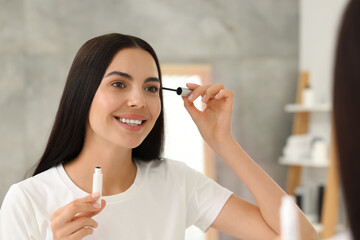 Poster - Beautiful woman applying serum onto her eyelashes indoors, reflection in mirror. Cosmetic product