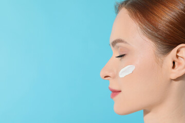 Poster - Beautiful young woman with sun protection cream on her face against light blue background, closeup. Space for text