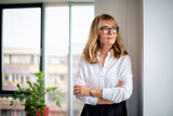 Fototapeta  - Thinking businesswoman standing with arms crossed at the office