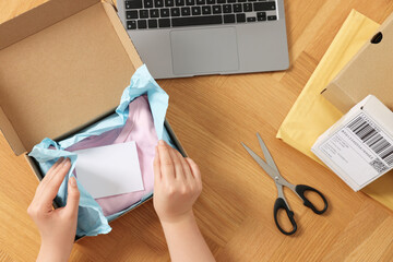 Canvas Print - Woman packing clothes at wooden table, top view. Online store