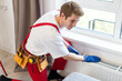 © Angelov - A plumber is fixing a radiator. With an adjustable wrench, he tightens the tap. A briefcase with a tool at hand