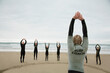 © fStop - Back view of a surfing instructor and a group of students stretching their arms on a beach