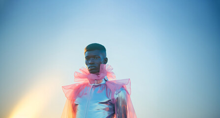 Haute couture fashion with a holographic twist, worn by a striking black androgynous model. Clear blue sky background. Futuristic and transcendent style.