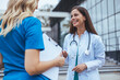 © Dragana Gordic - Two female doctor walk down an elevated walkway together. One wears a lab coat and the other wears scrubs. Female healthcare professionals walk and talk together
