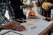 © MrAshi - Engineer points to building on blueprint and uses laptop to draw building design project in office Image engineer concept of engineer meeting for architectural project Work with partners