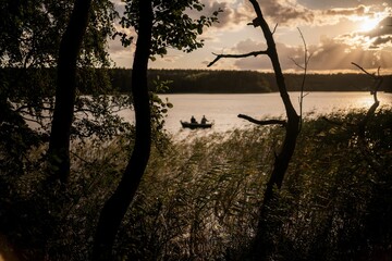 Wall Mural - Picturesque scene of a boat silhouetted against a beautiful sunset sky with lush trees.