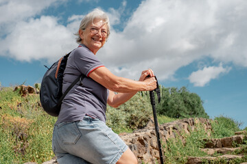 Sticker - Happy senior woman walking in a sunny day on trail outdoors on country excursion. Relaxed caucasian woman enjoying travel or retirement leading healthy lifestyle.