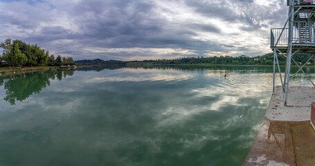 Wall Mural - Clairvaux-Les-Lacs, France - 09 03 2021: La Raillette, the big lake. Reflections of the cloudy sky and the landscape on the water of the lake..