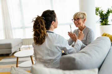 Wall Mural - Satisfied content patient feeling happy after receiving good news from female doctor at home visit while sitting on couch.