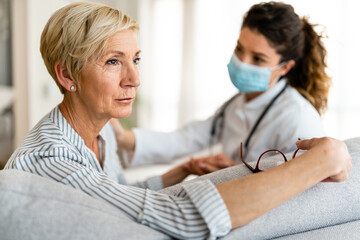 Wall Mural - Mature adult woman looking into the distance concerned about her medical test results while sitting with female doctor at nursing home.