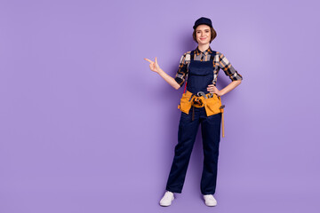 Wall Mural - Full length body size photo of woman engineer wearing cap overall pointing blank space isolated pastel violet color background