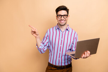 Wall Mural - Photo of young businessman wearing striped shirt hold netbook and pointing finger mockup hp electronics isolated on beige color background