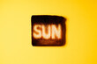 one burnt slices of white bread toast with the word Sun on it on yellow background. Sunbathing. creative concept composition representation danger of sun radiation and photo aging