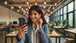 Hispanic female in co-working space on smartphone video call. Green plants and lights surround.