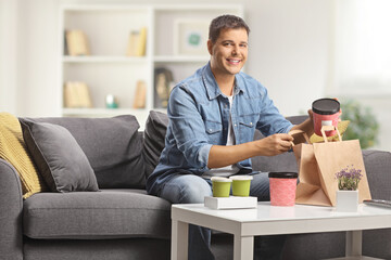 Poster - Young man sitting on a sofa with takeaway food boxes