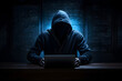 Hacker with a hoodie on sitting in front of a laptop in a dark room