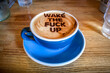 © Ulrike - A cup of morning coffee in a blue cup with saucer, with text 'wake the fuck up' in cacao powder on top.