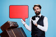 © DC Studio - Young doorman points at speech bubble against blue background, doing marketing ad using red billboard sign with copyspace. Concierge employee holding blank isolated cardboard on camera.