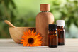 Bottles of essential oils and beautiful calendula flower on white wooden table outdoors, closeup