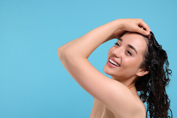 Wall Mural - Beautiful happy woman washing hair on light blue background. Space for text