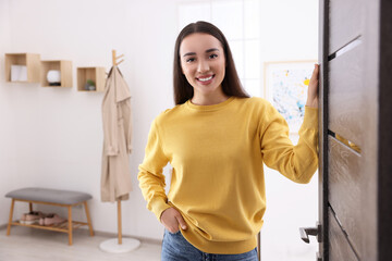 Wall Mural - Happy woman standing near door, space for text. Invitation to come indoors