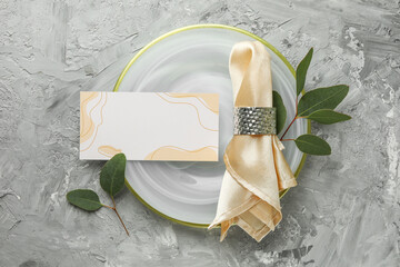Wall Mural - Blank invitation card, plate, napkin and eucalyptus leaves on grey table, flat lay. Space for text