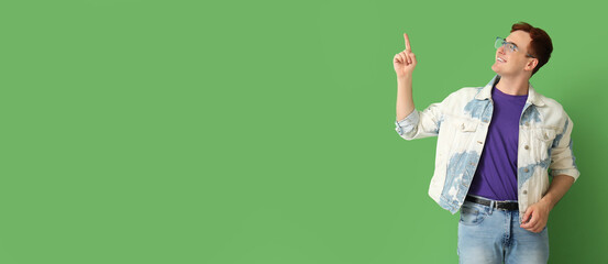 Poster - Happy young redhead man pointing at something on green background with space for text