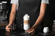 Barista holding glass of tasty latte with whipped cream in cafe