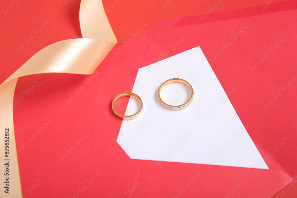 Envelope with greeting card, rings and golden ribbon on red background