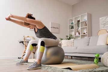 Poster - Beautiful young woman in sportswear exercising on fitness ball at home