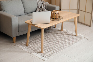 Interior of living room with stylish rug, laptop on coffee table and grey sofa