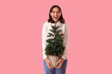 Wall Mural - Young woman in warm sweater with Christmas tree on pink background