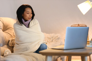 Wall Mural - Young Asian woman with warm plaid at home in evening