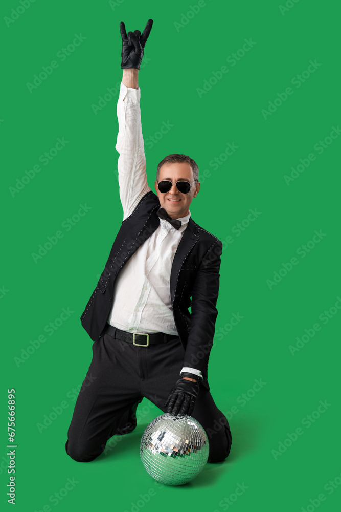 Cool mature man in suit with disco ball showing "devil horns" on green background