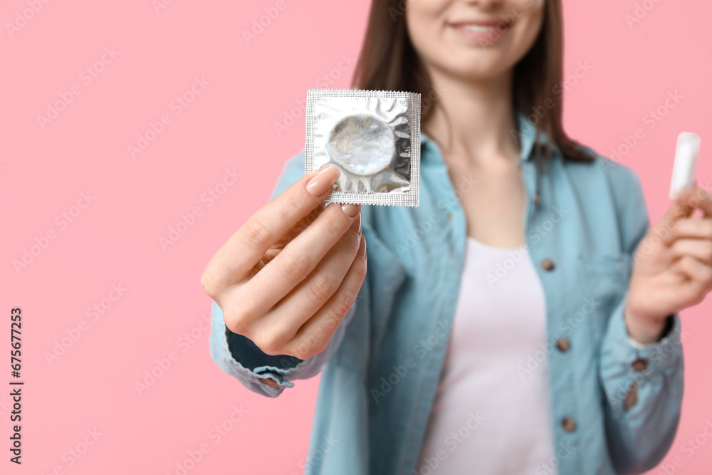 Beautiful young woman with suppository and condom on pink background. AID awareness concept