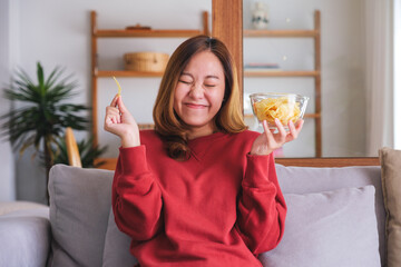 Wall Mural - Portrait image of a young woman picking and eating potato chips at home