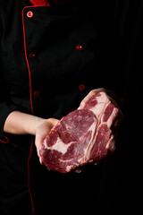 Wall Mural - The chef is holding a ribeye beef steak. Aged and matured steak. Meat. On a black background.