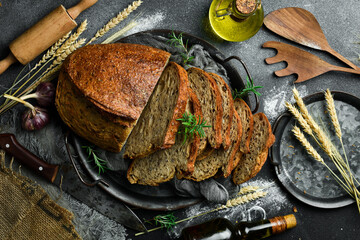 Wall Mural - Sourdough rye bread with flax cut on a board. Fresh bread on a black background. Top view.