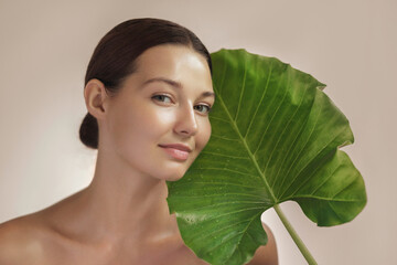 Wall Mural - Natural cosmetics skincare beauty product or treatment for female. Woman with beautiful face and healthy facial skin with big tropical green leaf.