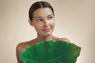 Wall Mural - Natural cosmetics skincare beauty product or treatment for female. Woman with beautiful face and healthy facial skin covering her body by big tropical green leaf.